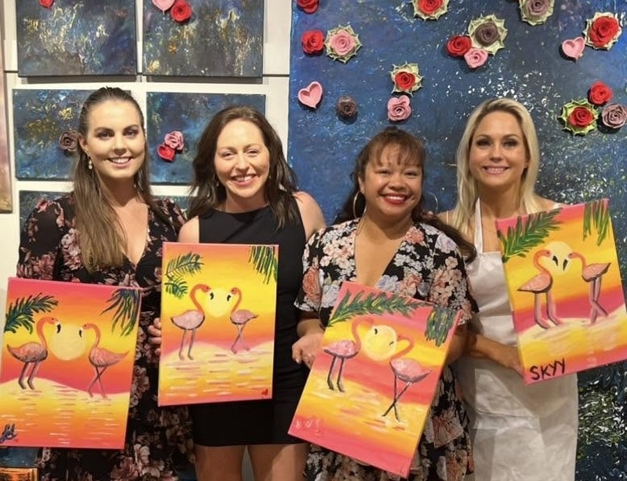 Four friends proudly holding up their flamingo sunset paintings