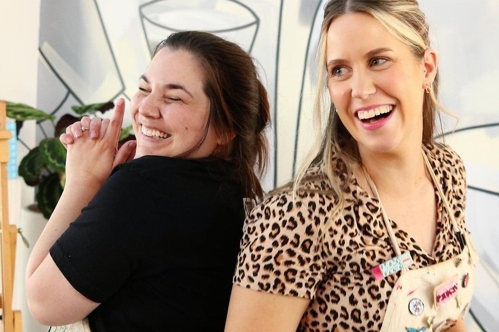 Two friends in aprons laughing together at a painting workshop
