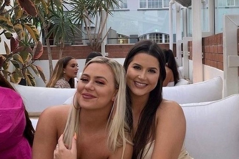 Two friends hugging on a white lounge at a rooftop bar