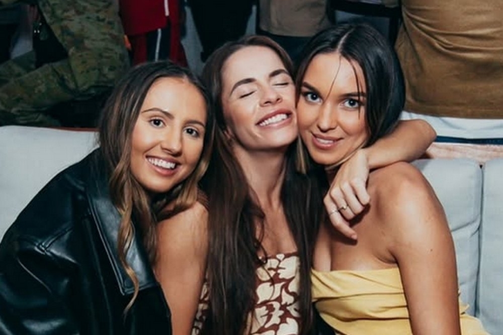 Three friends hugging and smiling in a plush booth