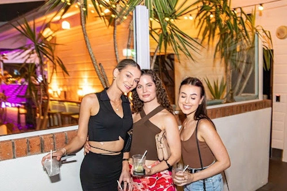 Three friends with drinks at a tropical bar lit up among the palms at night
