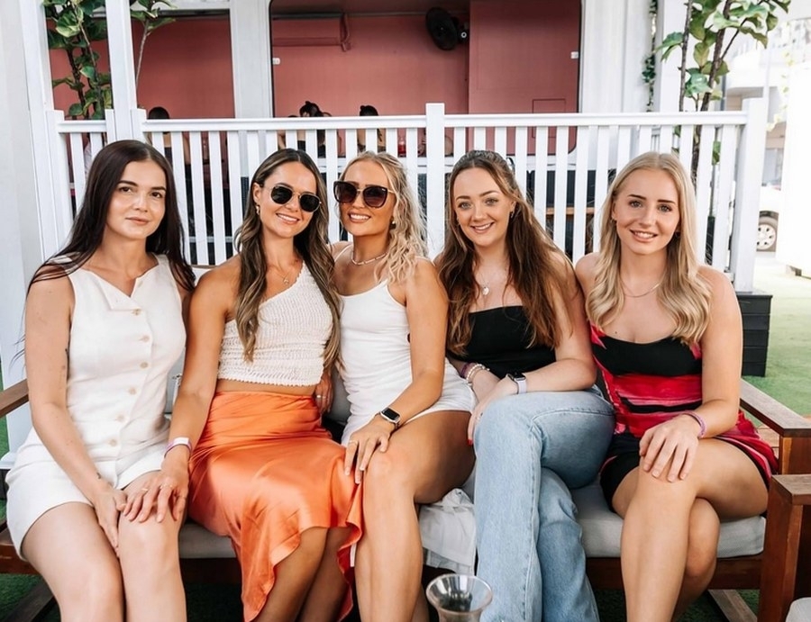 Five friends in sunglasses sitting close together on a white railed verandah