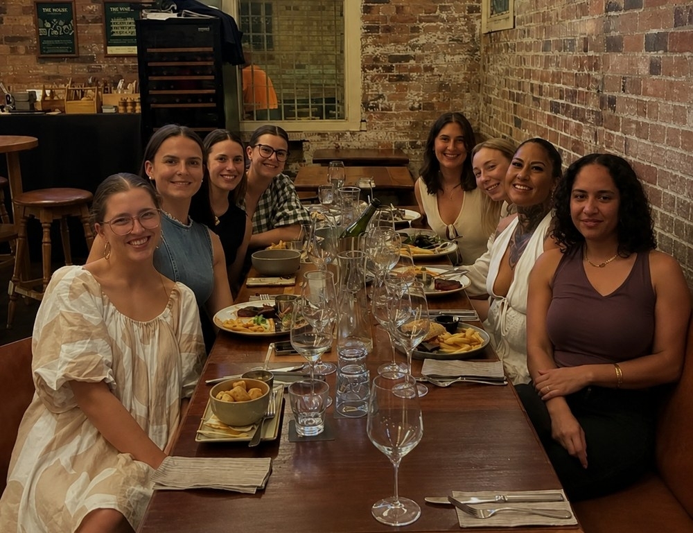 The girls smiling along a long timber table in a heritage brick pub