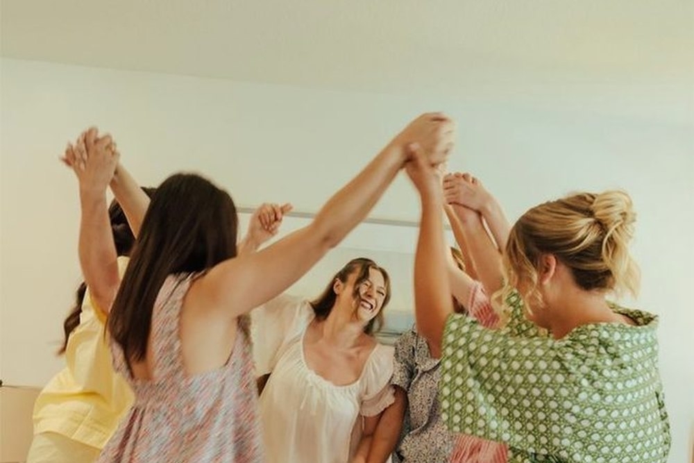 Friends in pyjamas dancing on the bed holding hands