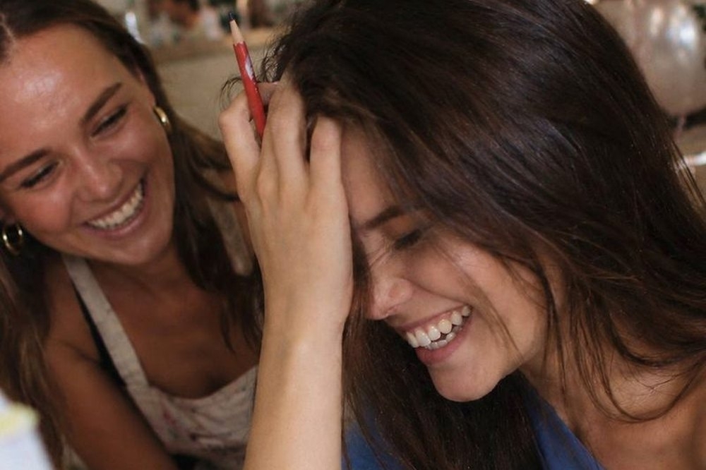 Two friends in aprons laughing together at the creative workshop table