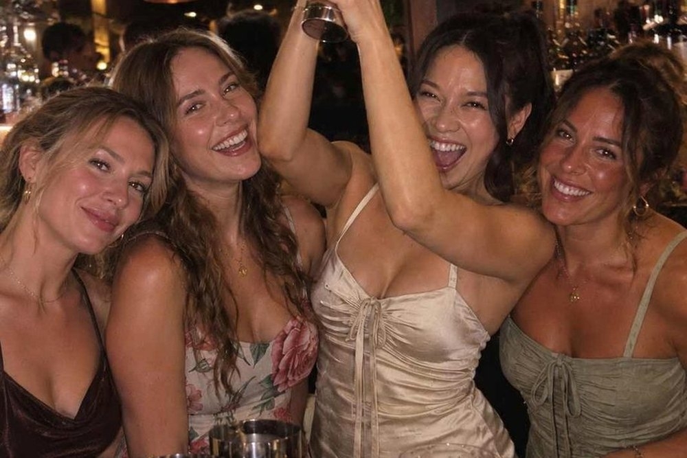 The girls laughing as one friend shakes her cocktail behind the bar