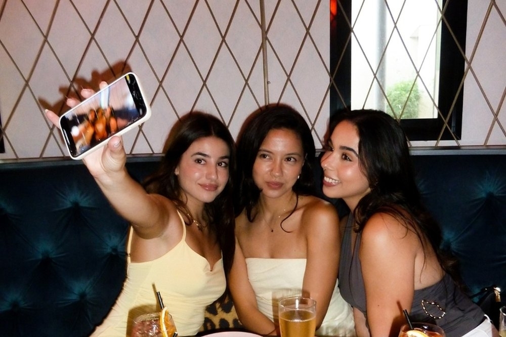 Four friends with colourful cocktails snapping a selfie in a velvet booth