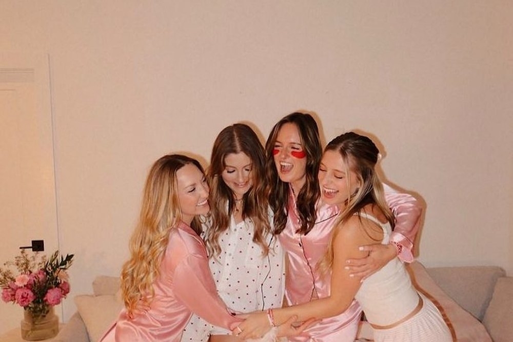 Four friends in satin pyjamas hugging and laughing by the couch