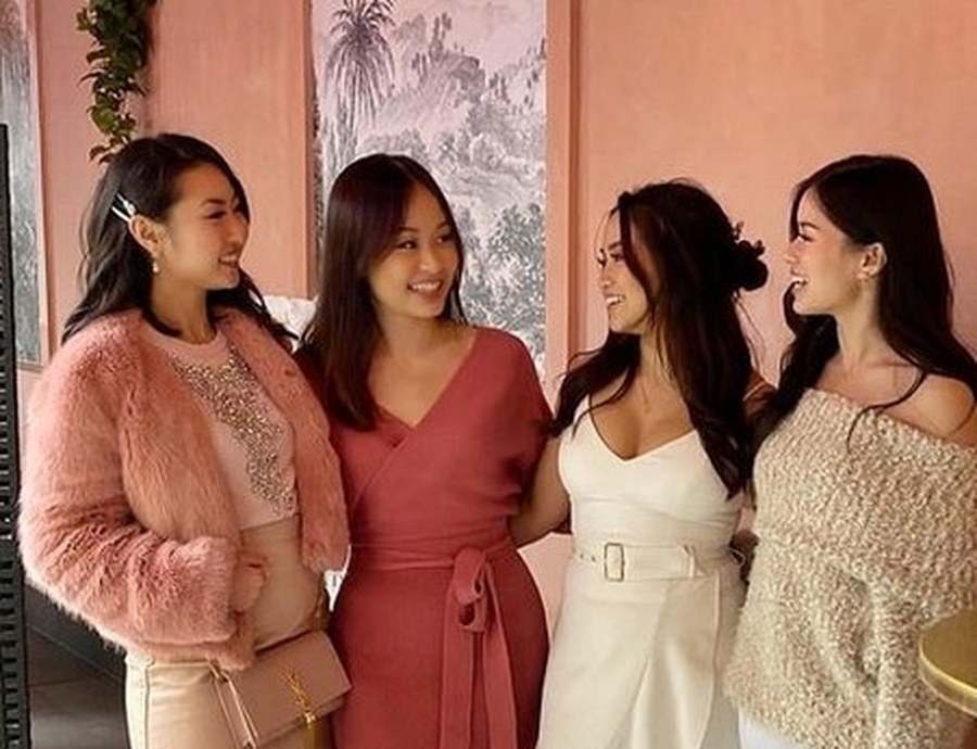 Four friends laughing together against pink walls and palm wallpaper