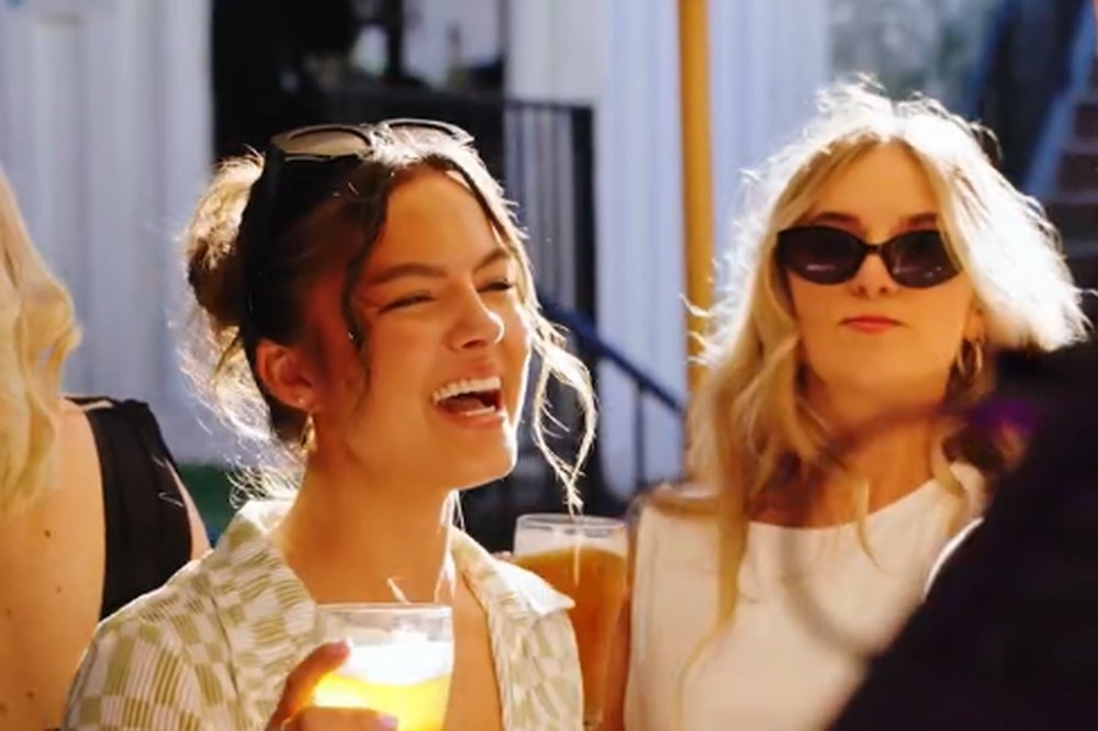 A friend laughing with a drink beside her friend in sunglasses