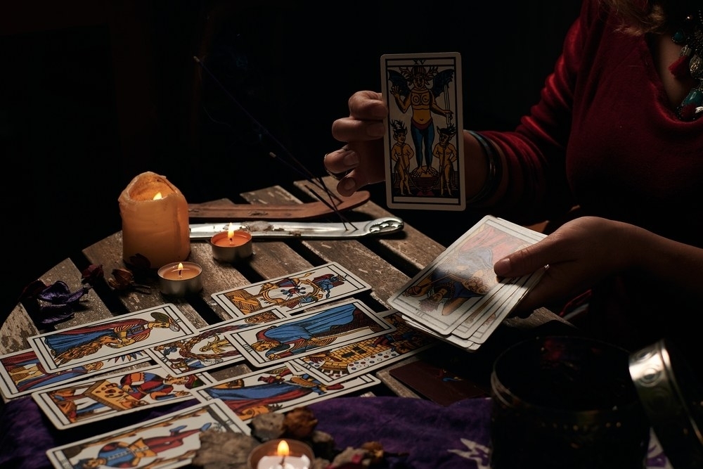 A reader laying out tarot cards by candlelight on a dark table