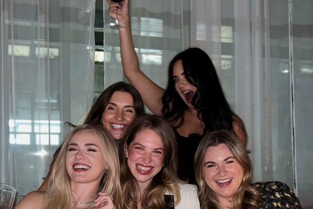Five friends laughing together around a restaurant table at night