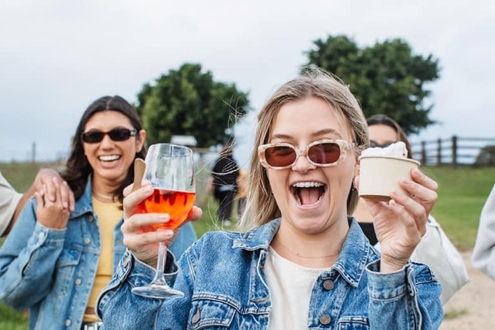 Friends in denim jackets laughing and raising their glasses outdoors