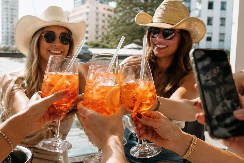 Friends in cowboy hats clinking drinks on a sunny terrace