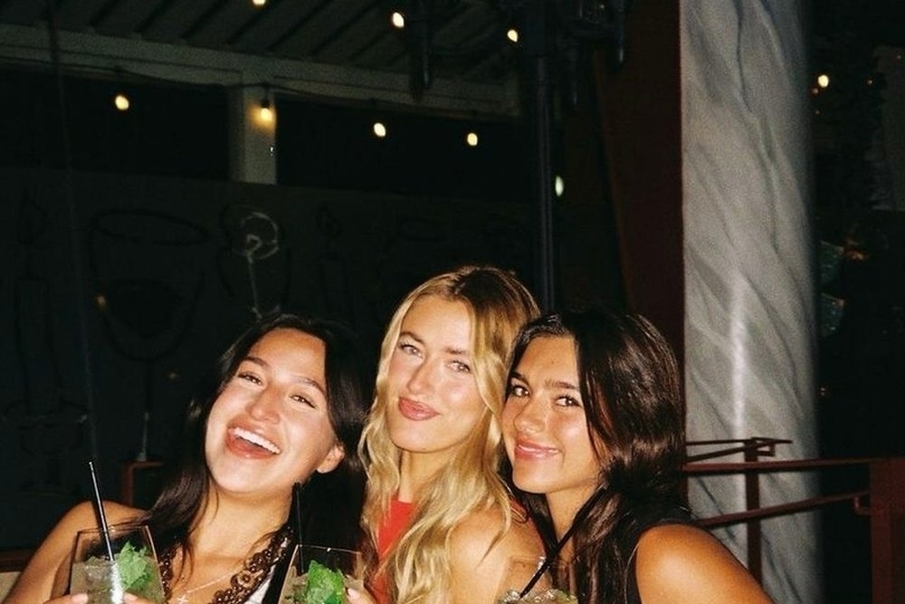 Three friends laughing together with drinks at an outdoor bar at night