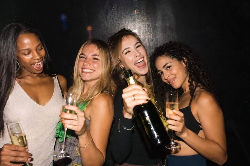 Four friends laughing with a bottle of bubbly and flutes on a night out