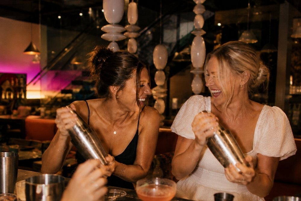Two friends laughing as they shake cocktails at the bar