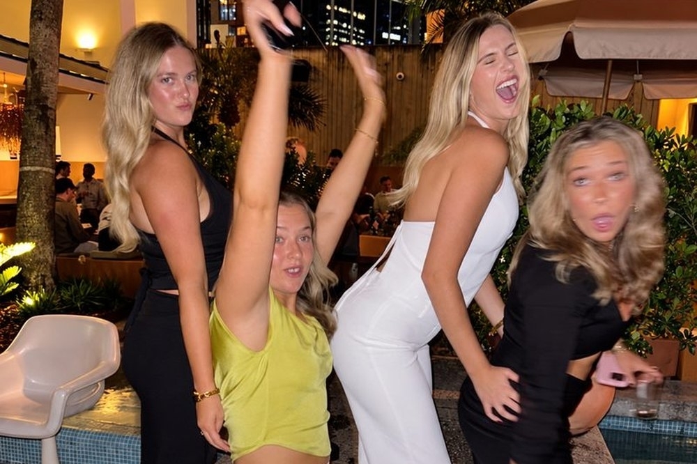 Four friends dancing and pulling faces on a palm lined terrace at night