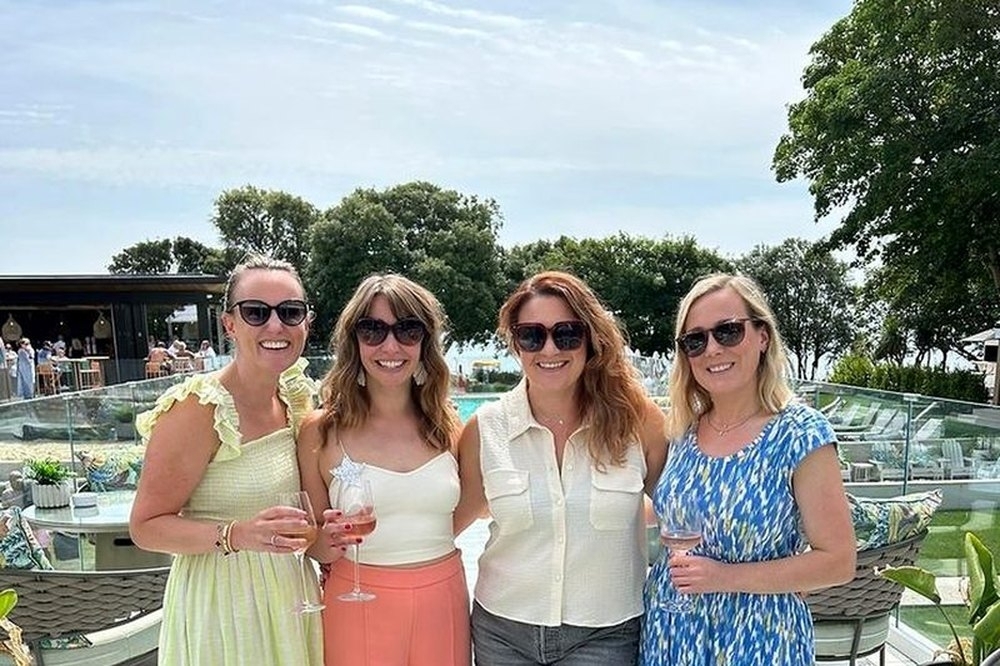Four friends in summer outfits posing together on a sunny rooftop terrace