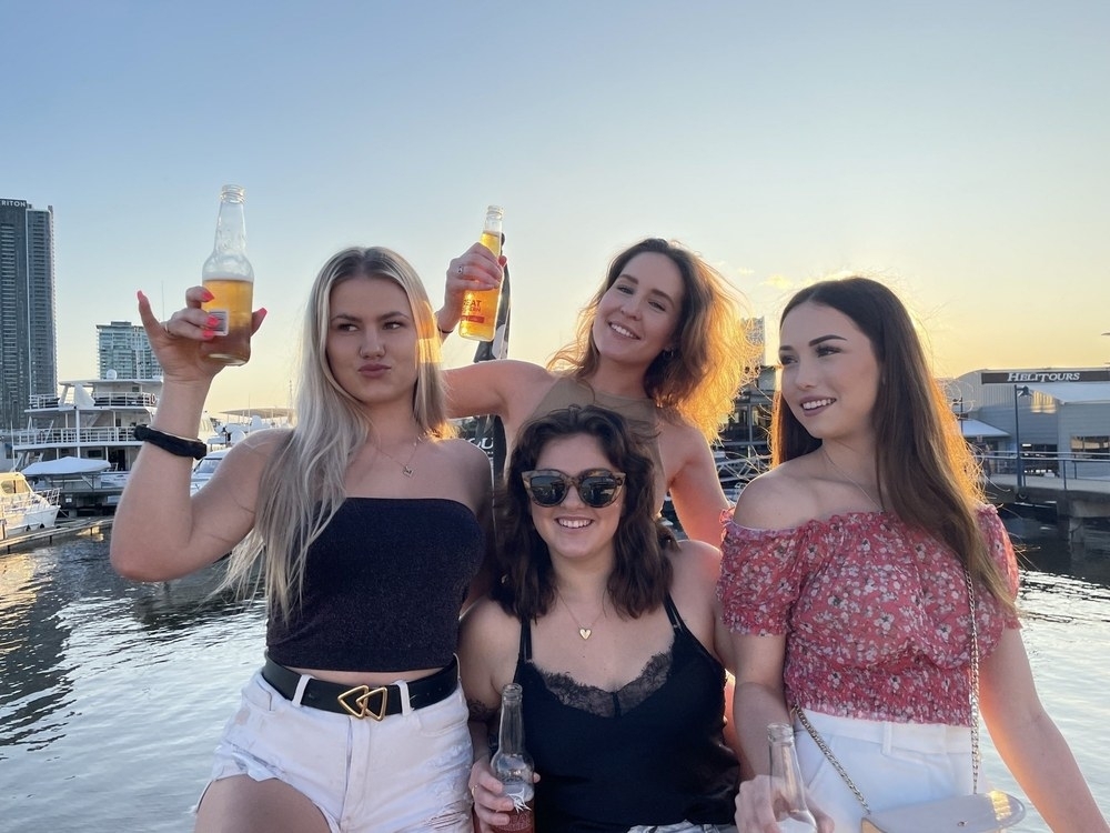Four friends raising drinks together on the water at sunset
