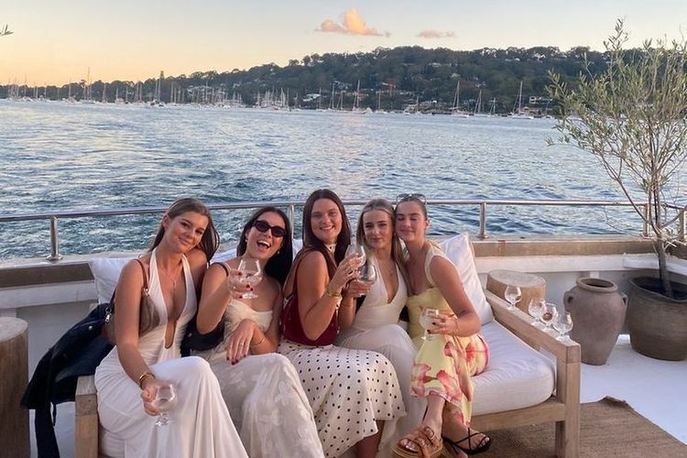 Five friends in summer dresses relaxing together on a waterfront terrace at sunset