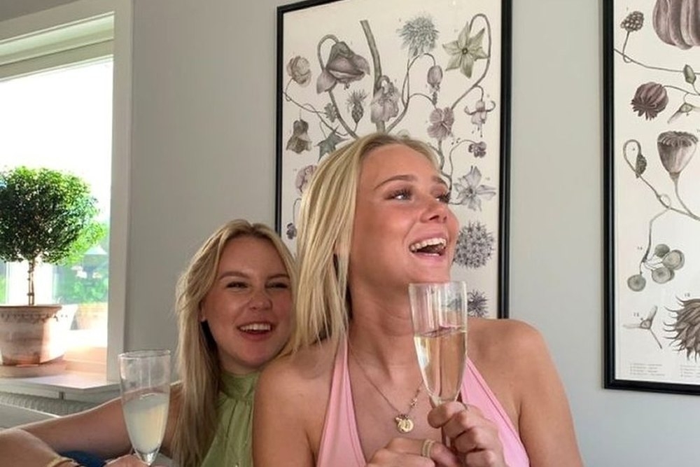 Two friends laughing with bubbly on the couch in a bright apartment