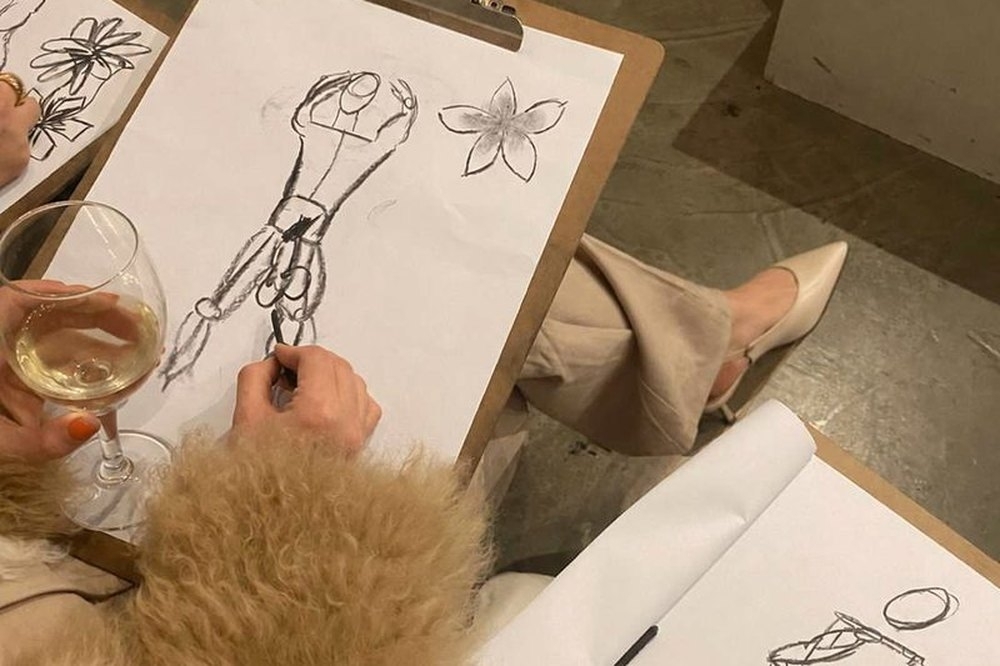 Life drawing sketches on clipboards beside a glass of wine