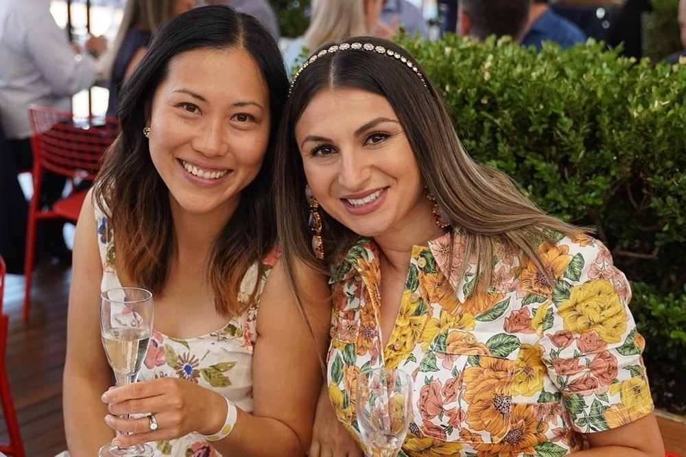 Two friends smiling with glasses of bubbly at a sunny restaurant table