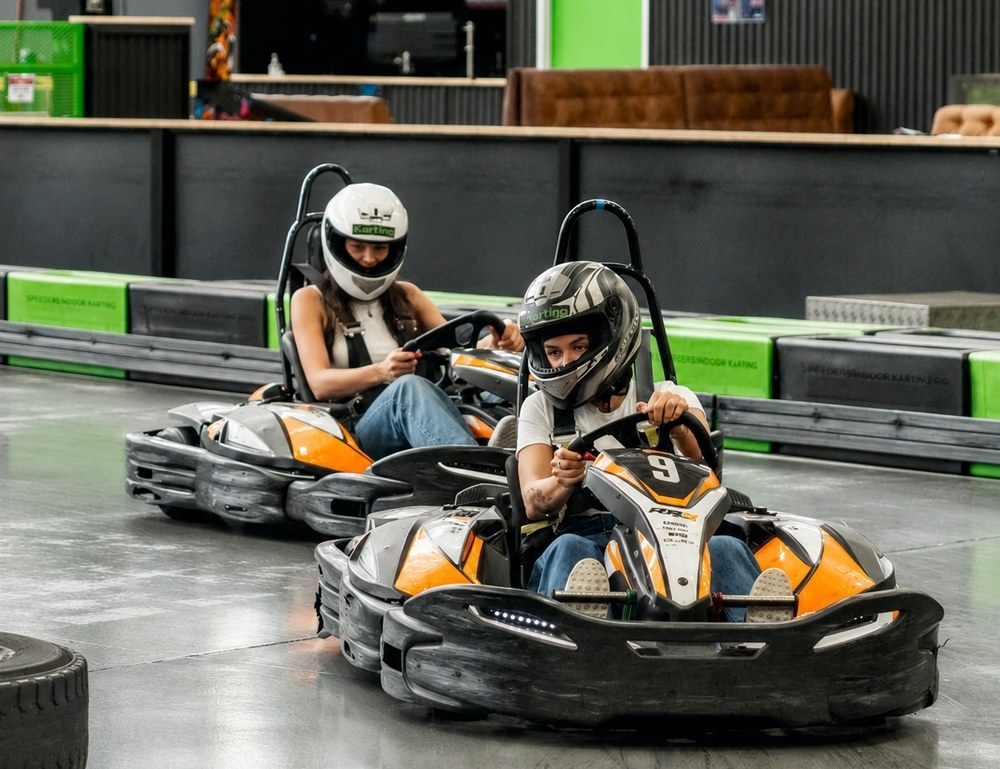 Two friends in helmets racing go karts around an indoor track