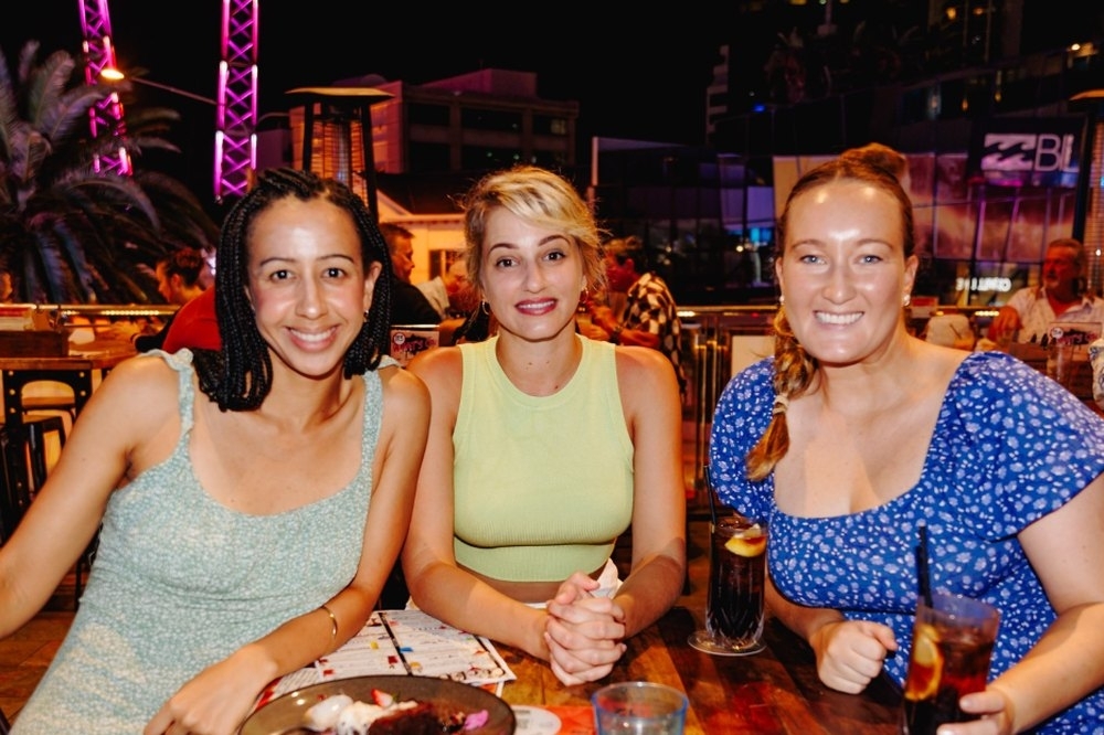 Three friends smiling at a restaurant table with drinks at dinner