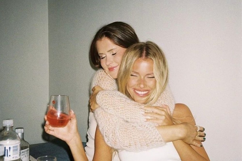Two friends hugging and laughing over drinks at the apartment