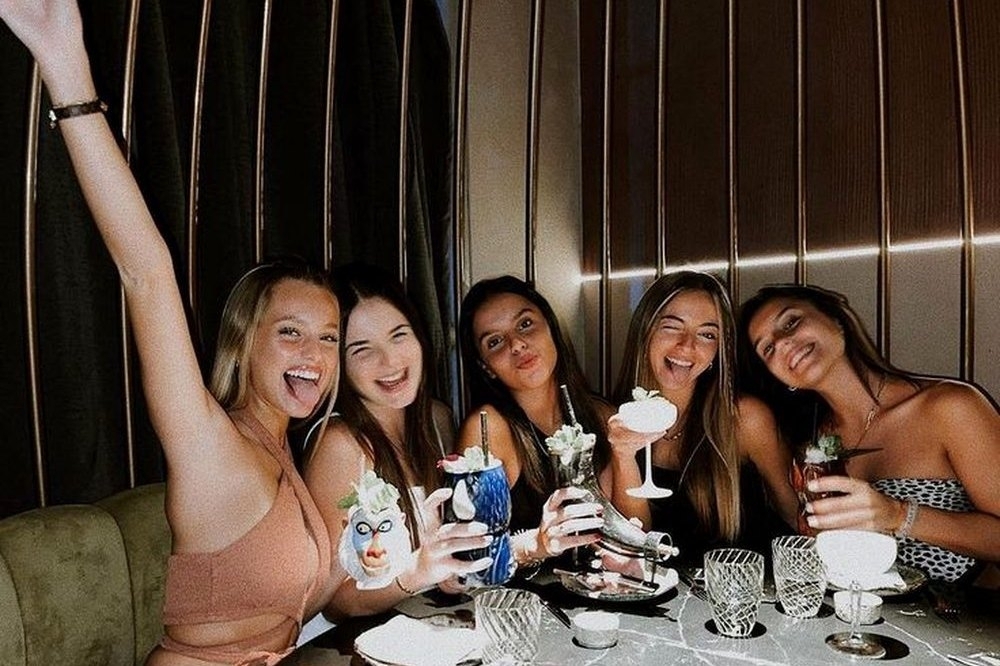 Five friends cheering with drinks around a restaurant table