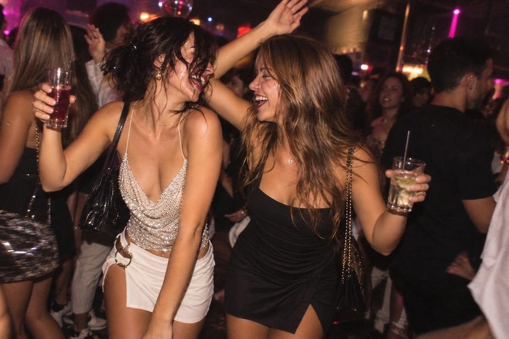 Two friends dancing with drinks in hand in a crowded nightclub