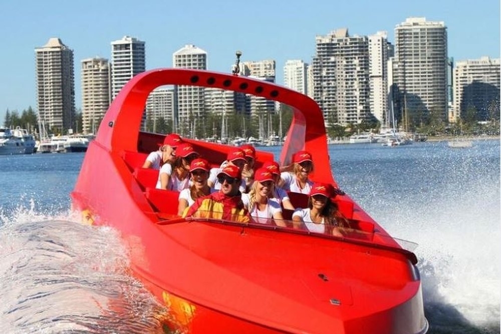 A red jet boat full of passengers spinning on the water in front of high-rise buildings