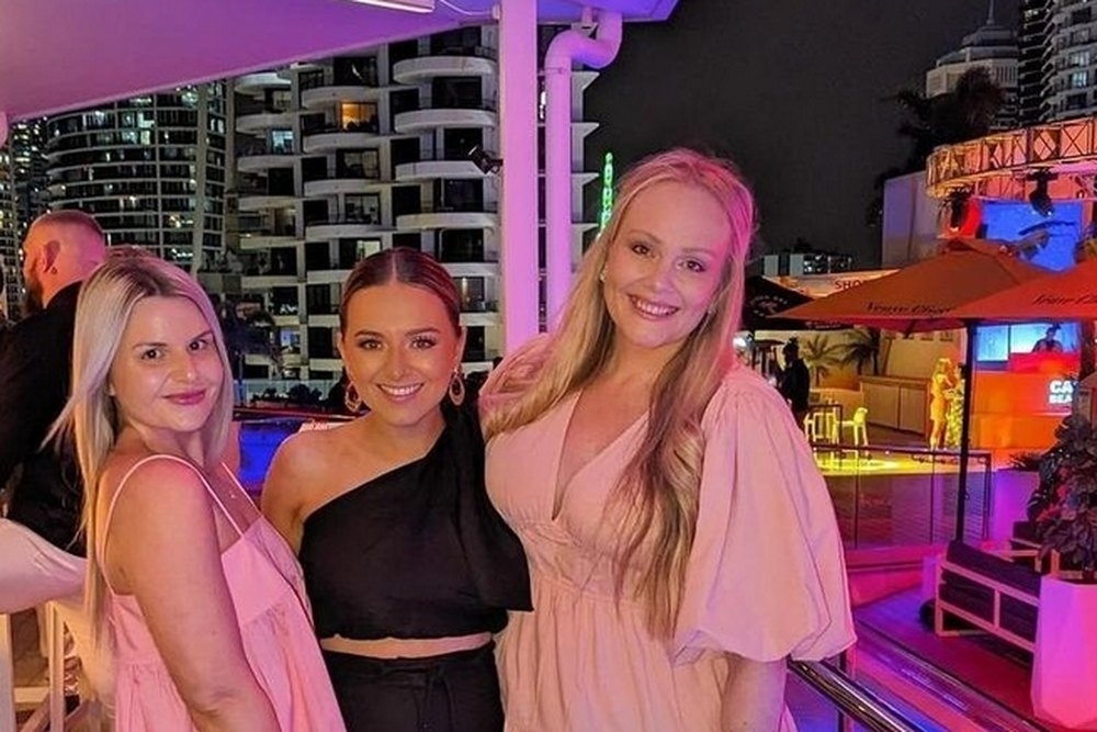Three friends posing together by the lit up waterfront at night