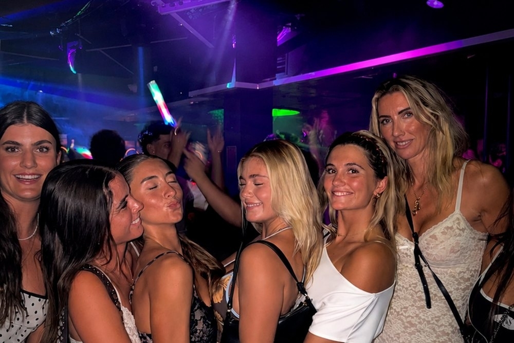 A group of friends squeezed together on a nightclub dance floor under coloured lights