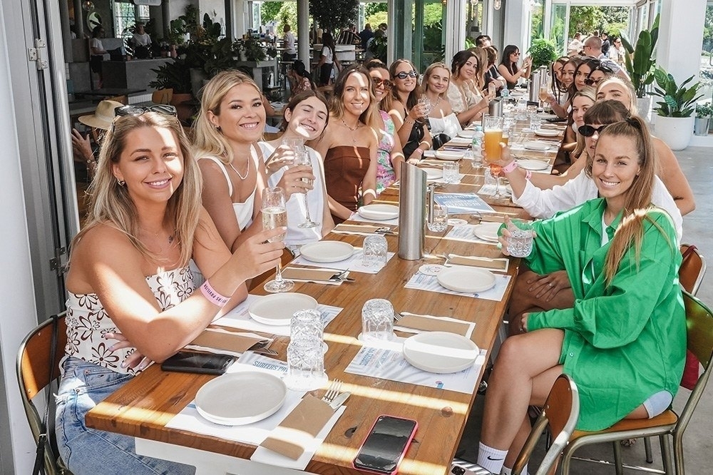 Friends smiling over mimosas at a long lunch table