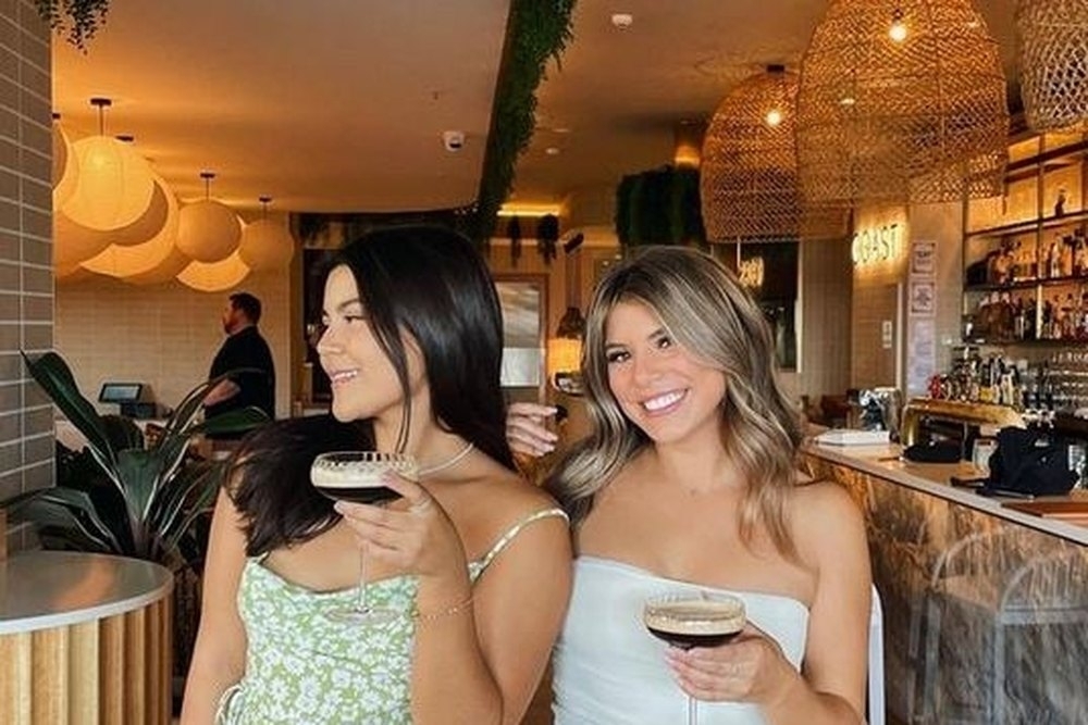 Two friends in summer dresses holding cocktails in a stylish bar