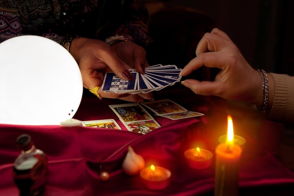 A reader fanning out tarot cards beside a glowing candle